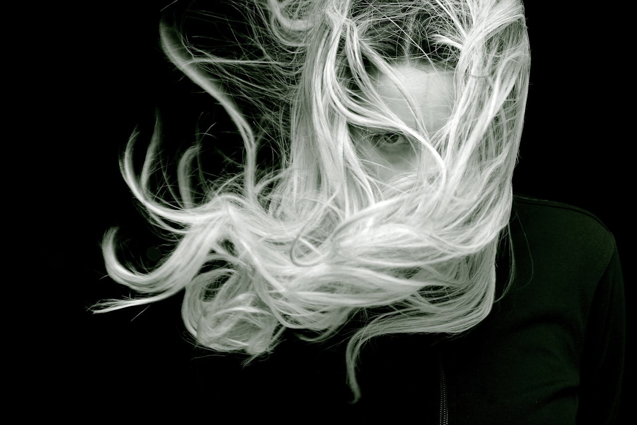 A striking black and white portrait of a woman with long, flowing hair that creates a sense of motion and mystery.